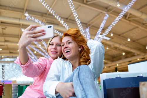 Two happy friends is taking selfie while shopping in mall.