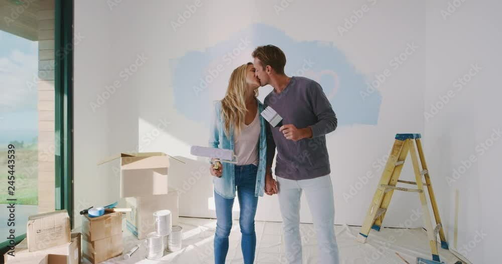 Cute happy couple kissing with paint brushes, happy new homeowners, home improvement