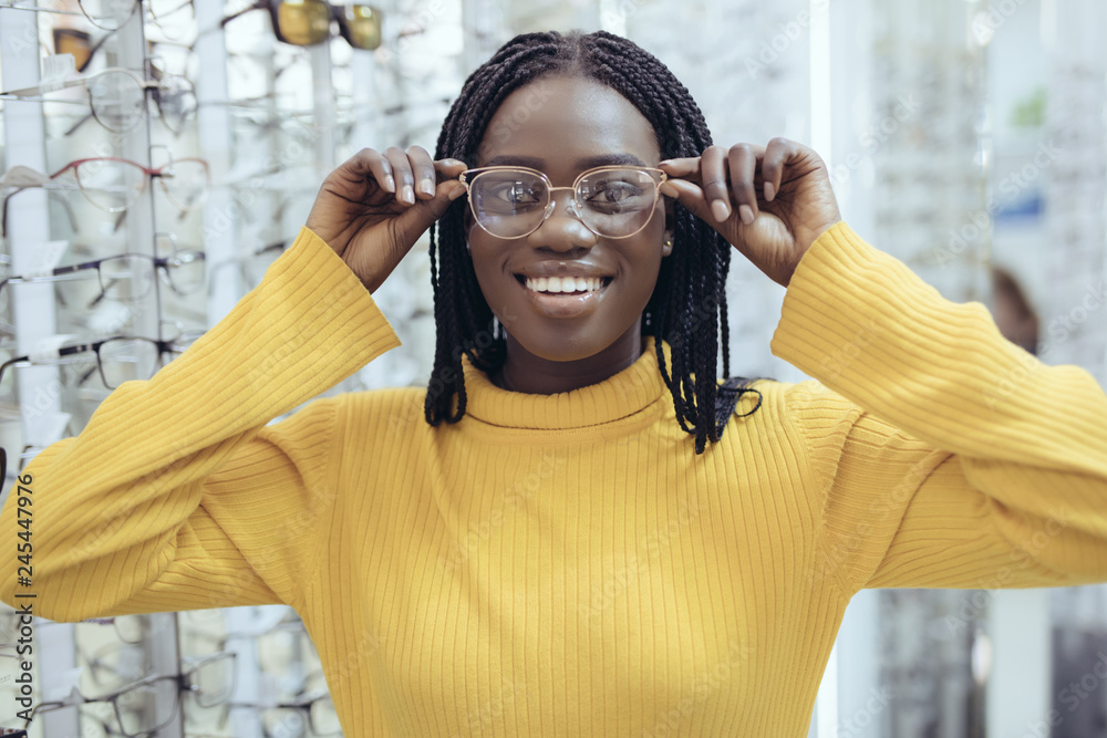 Young pretty african woman choosing prescription glasses frames in Optician's shop.