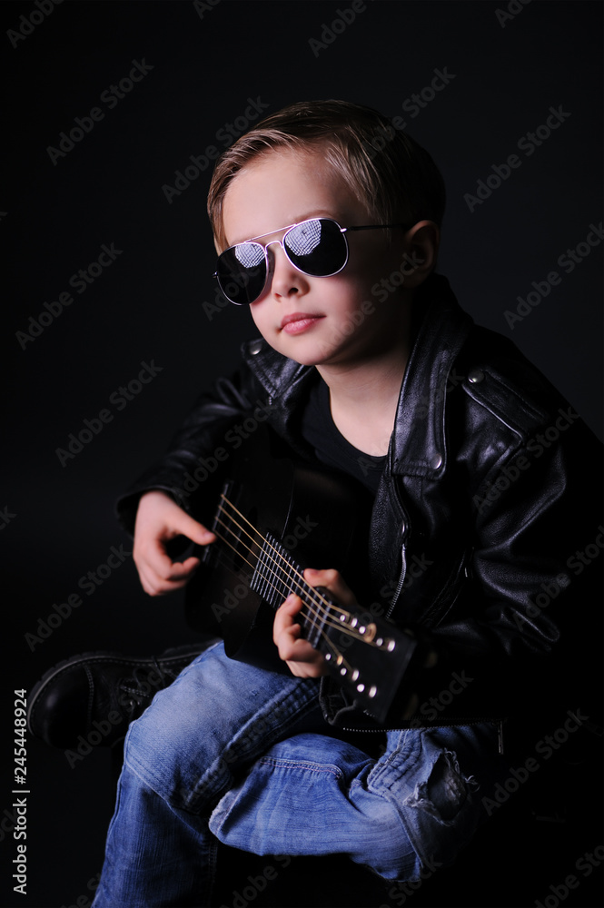 A boy dressed in black with dark glasses, playing the guitar. Clouse up, black background, studio shot. A boy dressed in black with dark glasses, playing the guitar. Clouse up, black background, studio shot.