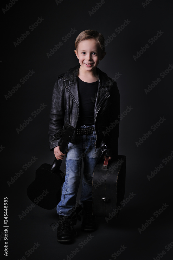 Smiling boy model on a black background in studio. Looking at camera,whole body. Dressed in black leather and jeans.
