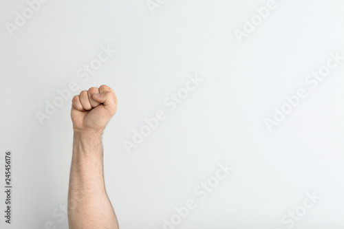 Young man showing clenched fist on light background. Space for text