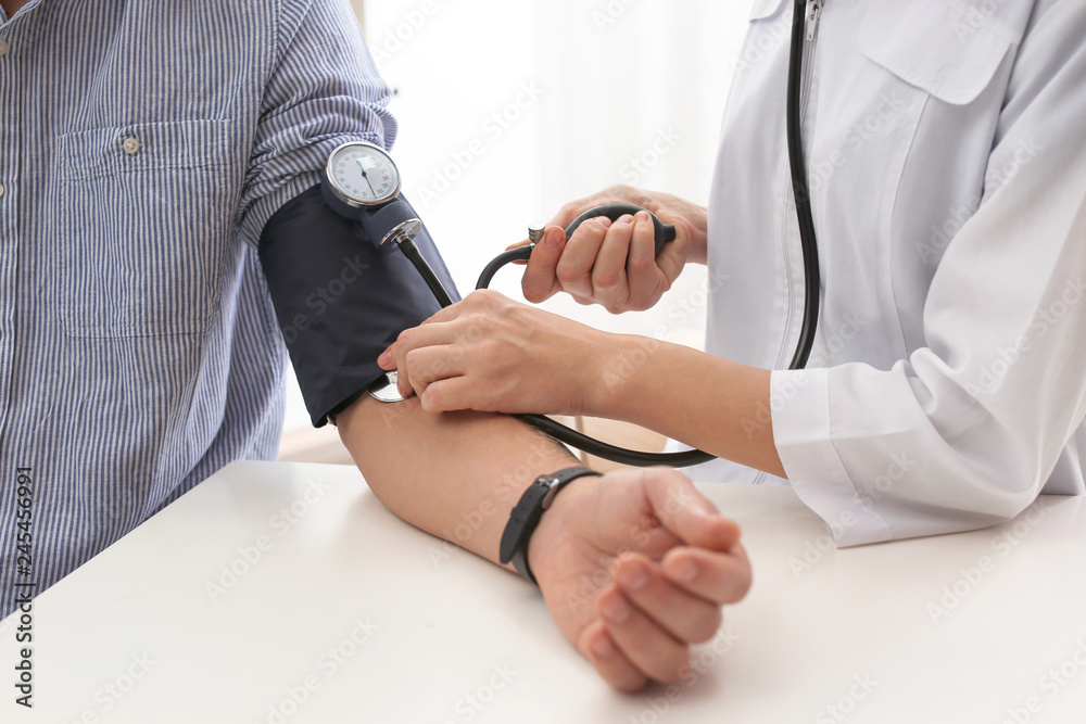 Doctor checking patient's blood pressure in hospital, closeup. Cardiology concept