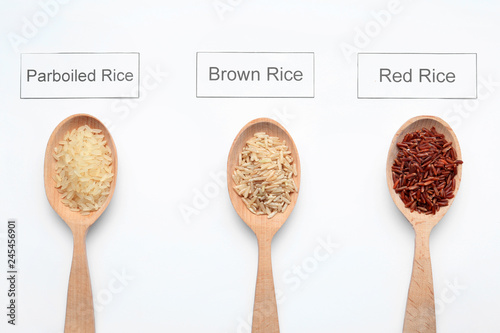 Spoons with different types of uncooked rice and cards on white background, top view