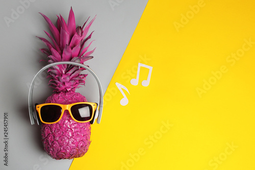 Pineapple with headphones and sunglasses on color background, top view with space for text