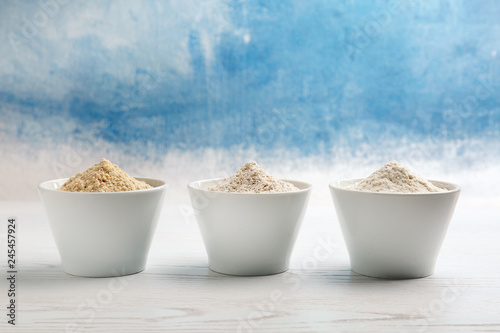 Bowls with different types of flour on table against color background. Space for text