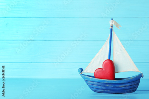 Toy boat with red heart on table against color background. Space for text
