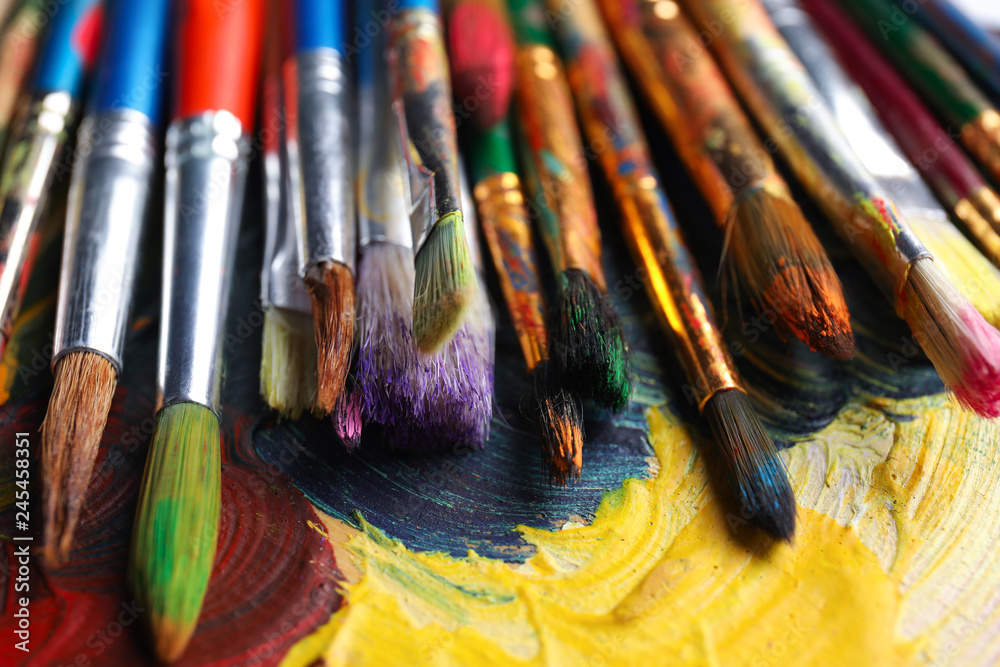 Fototapeta premium Different paint brushes on color palette, closeup