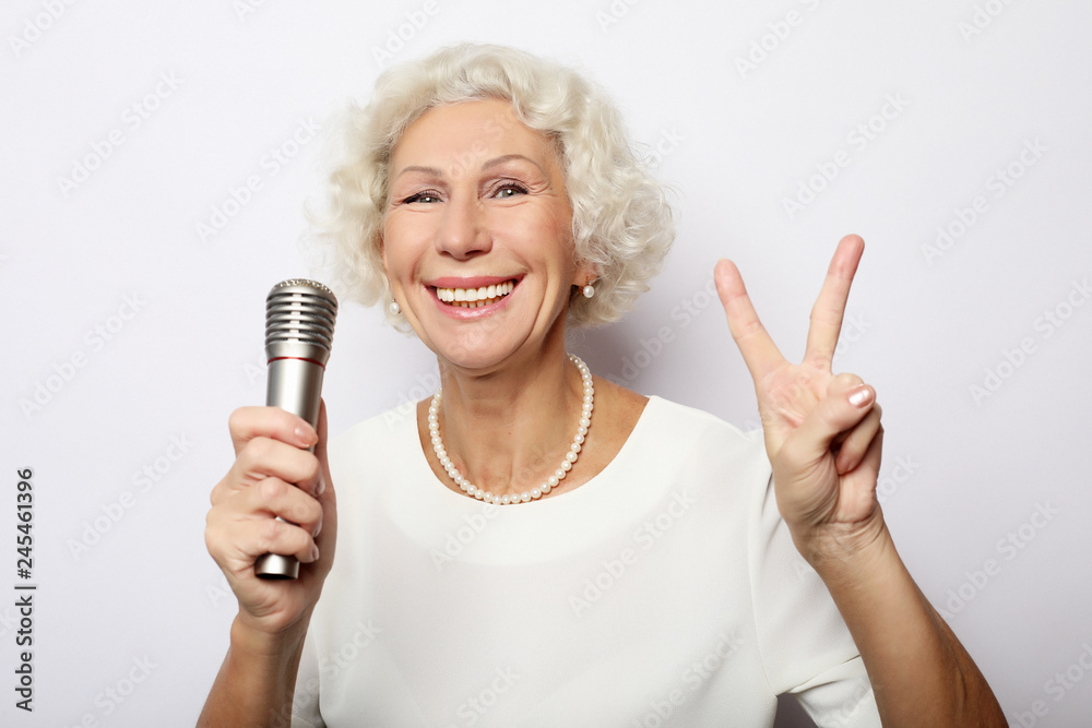 Portrait of charming modern grandmother holds up the microphone stand and sings Portrait of charming modern grandmother holds up the microphone stand and sings