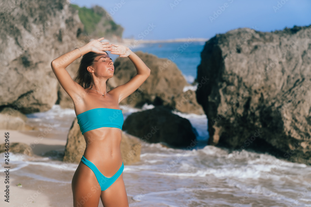 Sexy tanned girl in blue swimsuit posing on sunny day at sandy beach