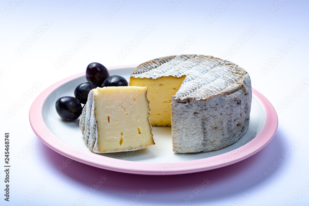 Round mature French Tomme cheese with one cutted piece close up isolated
