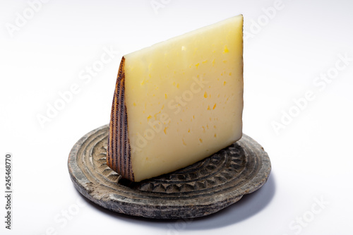 Piece of Spanish hard scheep milk cheese Manchego on grey stone plate isolated close up