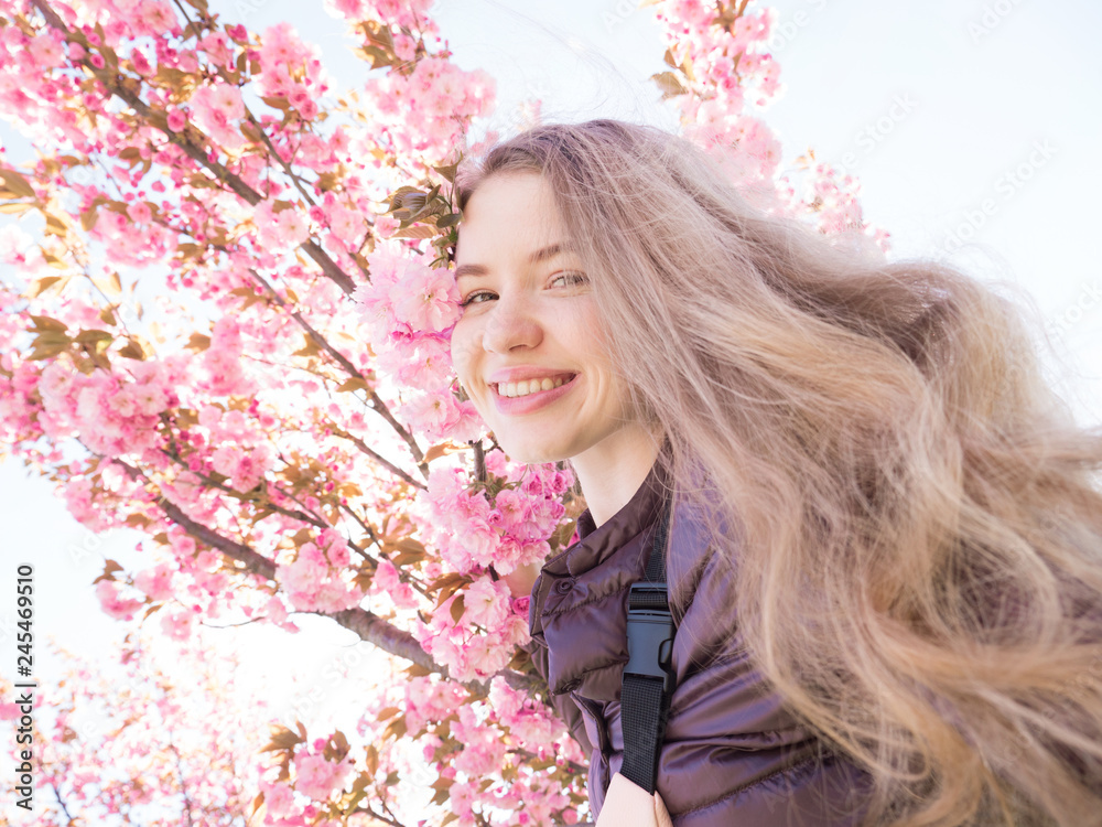 Woman with gorgeous smile having fun in blooming garden. Girl with long hair outdoor, cherry blossom on background. Perfume and fragrance concept. Woman enjoy aroma of spring day.