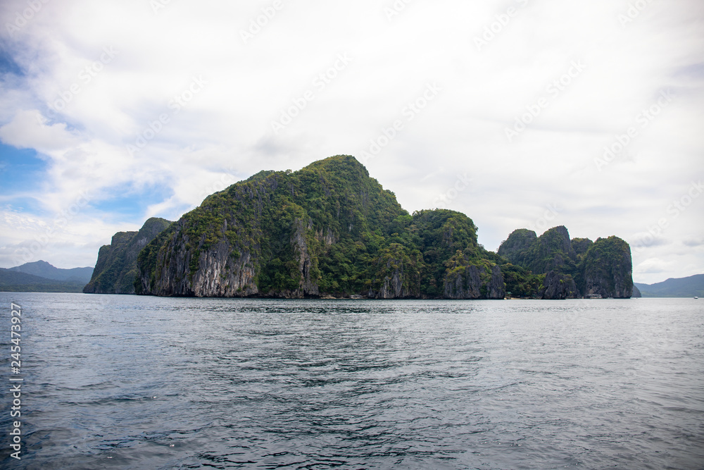 Tropical seaside with still sea water and abandoned island. Black rocks ith green forest in sea. Natural landscape Tropical seaside with still sea water and abandoned island. Black rocks ith green forest in sea. Natural landscape