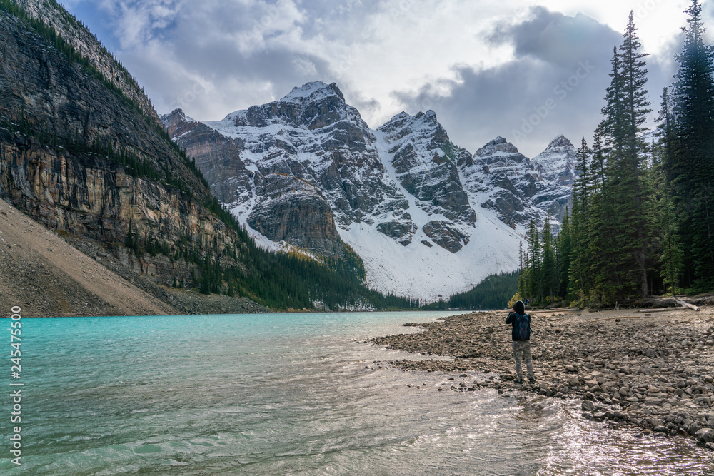 Moraine Lake under cloudy sky with a traveller taking photography