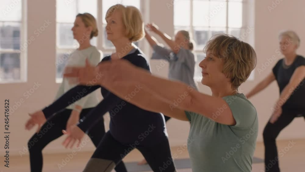 yoga class healthy mature woman practicing warrior pose enjoying group workout in fitness studio
