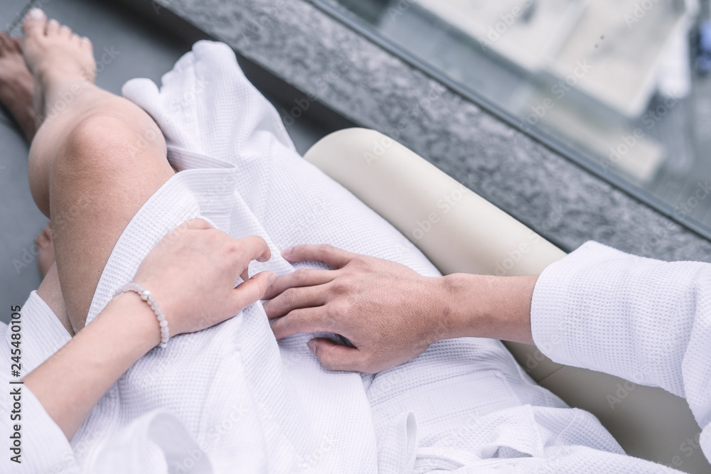 Obraz premium Woman sitting on man's laps in white hotel robes touching each other hands. Overhead, man's and woman's legs from above. Intimacy, Valentine's day concept