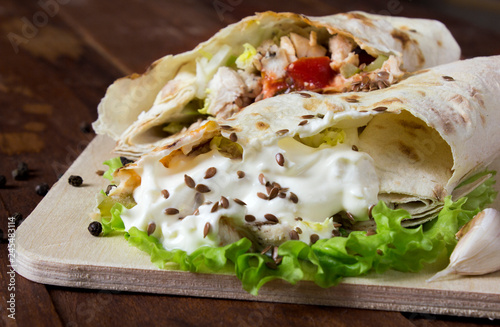 Shaurma chicken roll in a pita with fresh vegetables and cream sauce composition on wooden background