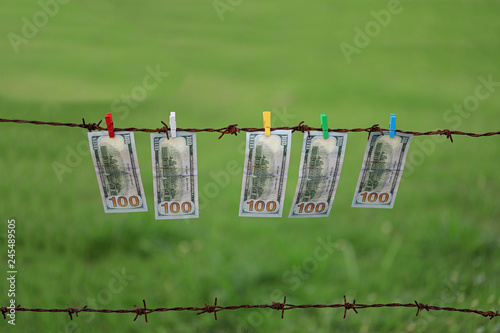 Money Laundering. Money Laundering US Dollars Hung Out To Dry. 100 Dollar Bills Hanging On Rusty Barbed Wire photo