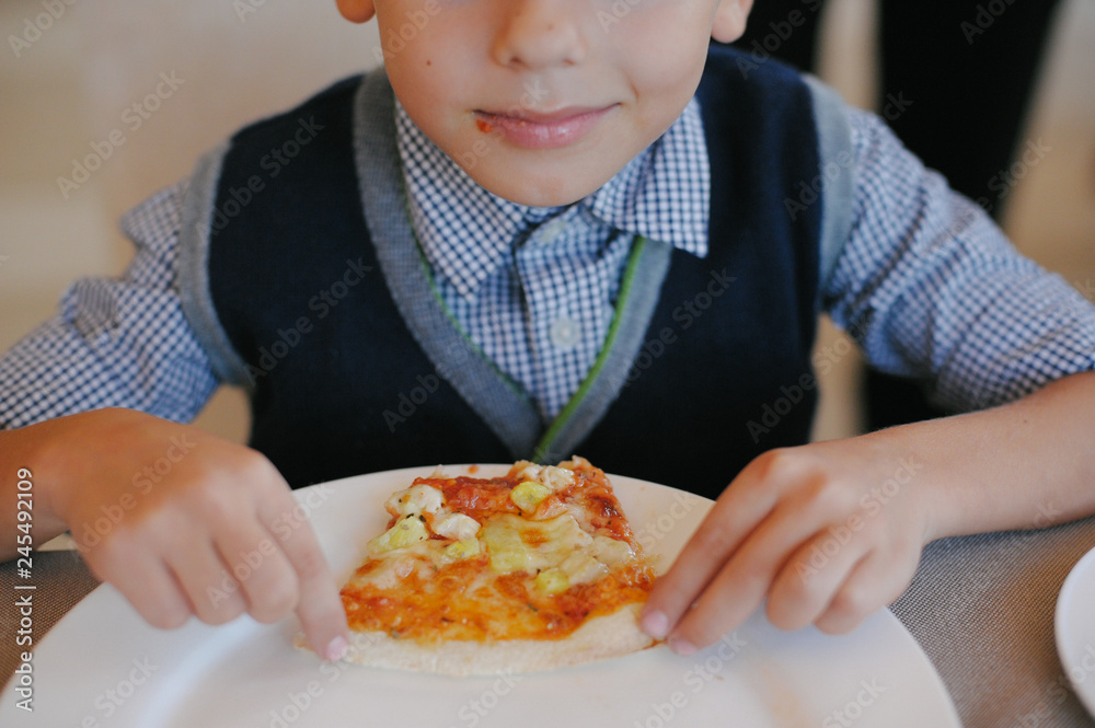 happy little boy holding and eating pizza in cafe