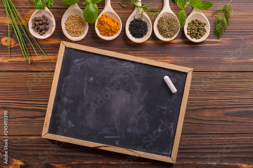 Mixed spices and herbs on wooden spoons with blackboard.
