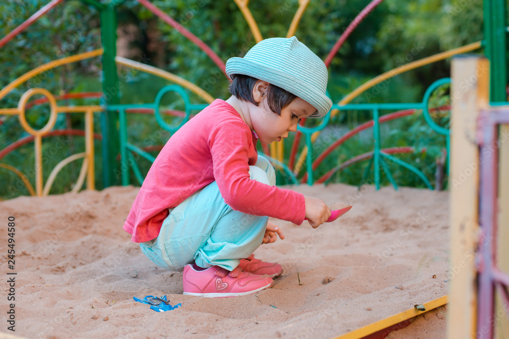 A little girl likes to play on the playground sandbox. Children's fun physical development in the open air.