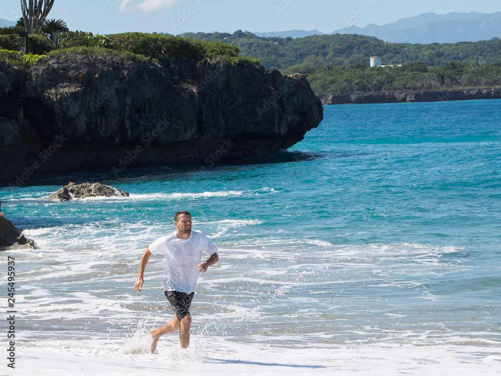 A man runs along the beach of the ocean. Sunny day and big waves.