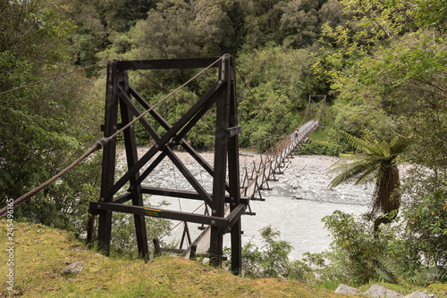 Tourist hikers crossing the Douglas Bridge suspension bridge across the Waiho River in the Franz Josef valley, Westland National Park/Tai Poutini National Park, New Zealand. photo