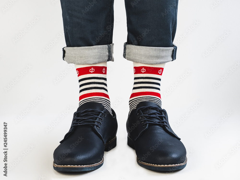 Men's legs, bright, striped, multicolored socks with a nautical theme and shoes on a white, isolated background. Close-up. Concept of style, fashion and beauty