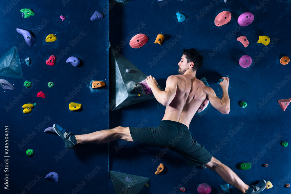 Fototapeta premium Successful self confident muscle healthy winner climber mountaineer alpinist man male bouldering training in climbing wall. Achieved top of wall in complex competition. Success and healthy lifestyle