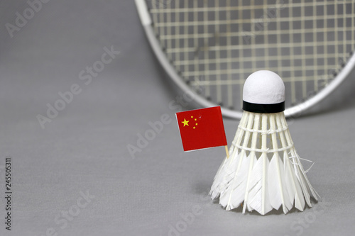 Mini China flag stick on the white shuttlecock on the grey background and out focus badminton racket.