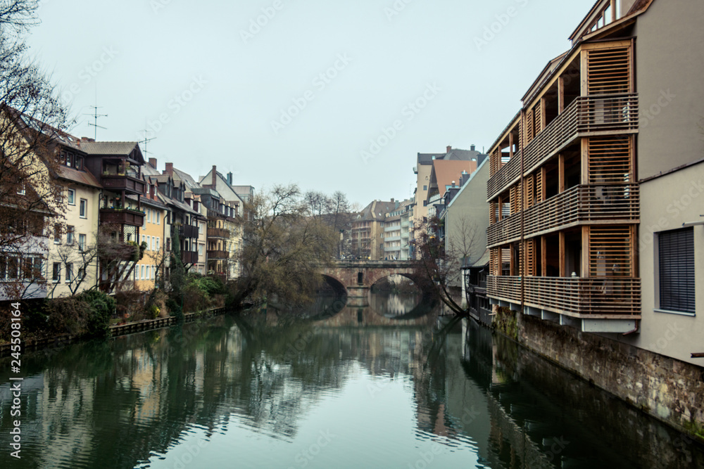 Houses and a bridge reflected in a river in the old town of Nuremberg / Nürnberg during winter with moody sky (Nuremberg, Germany, Europe)