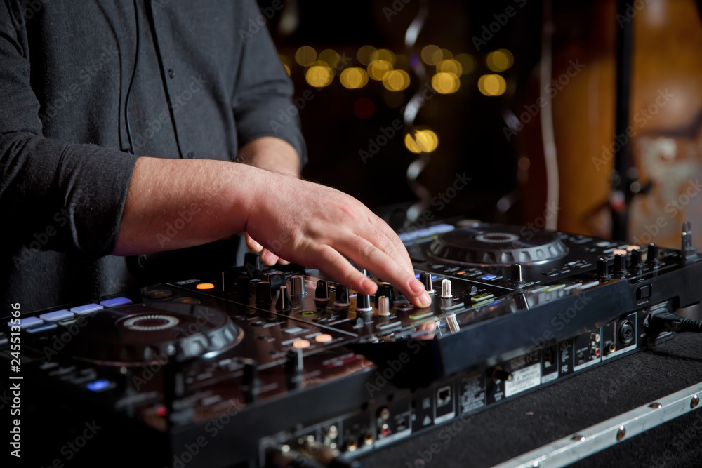 Dj mixes the track in the nightclub at party. Headphones in foreground and DJ hands in motion . Club party dj plays live set on stage in nightclub.