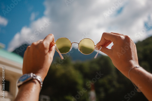 Hands holding yellow round sun glasses over blue sky photo