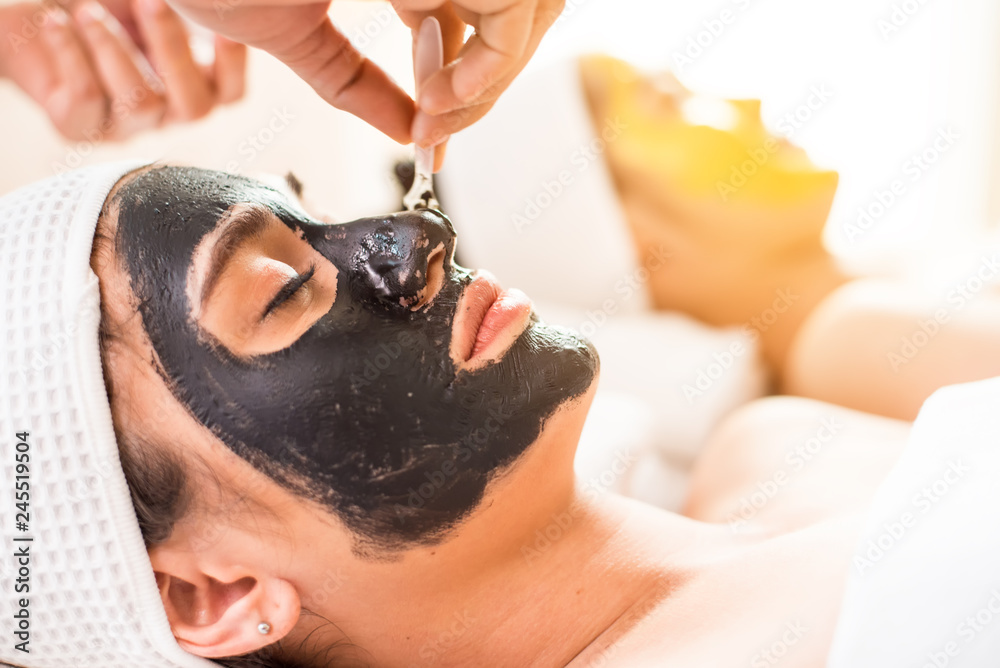 Naklejka premium Close up of Healthy Young Woman getting mud Black and gold facial mask cosmetic procedure in the beauty salon.Skin treatment in spa salon concept