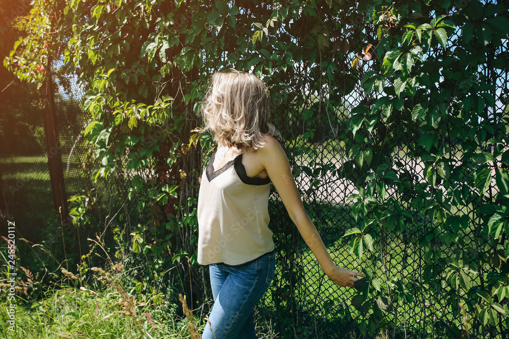 Stylish hipster girl is standing near the ivy leaves wall outdoors. Fashionable photoshoot for young women. Blonde short hair and cool glasses. Summer lifestyle photoshoot. Stylish hipster girl is standing near the ivy leaves wall outdoors. Fashionable photoshoot for young women. Blonde short hair and cool glasses. Summer lifestyle photoshoot.