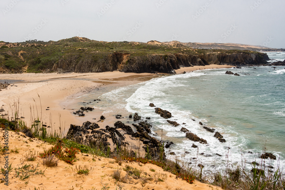 Wild sandy beach with cliffs on Atlantic ocean coast, Atlantic Ocean, Rota Vicentina, Alentejo, Portugal. Small waves hitting the rocks.