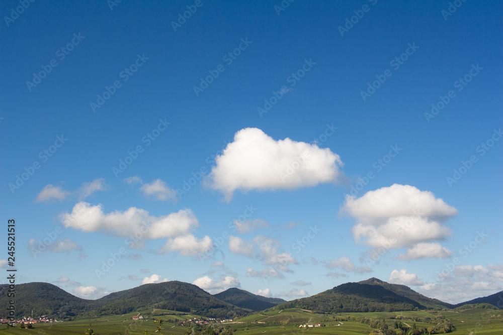 Idyllische Hügellandschaft unter blauem Himmel mit weißen Wolken Idyllische Hügellandschaft unter blauem Himmel mit weißen Wolken