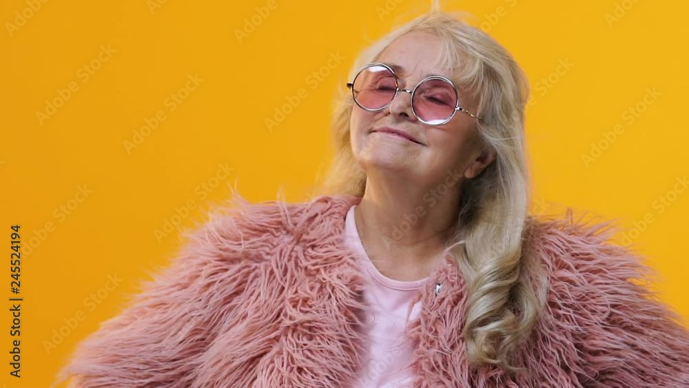 Positive grandmother moving on bright yellow background, style and fashion Positive grandmother moving on bright yellow background, style and fashion