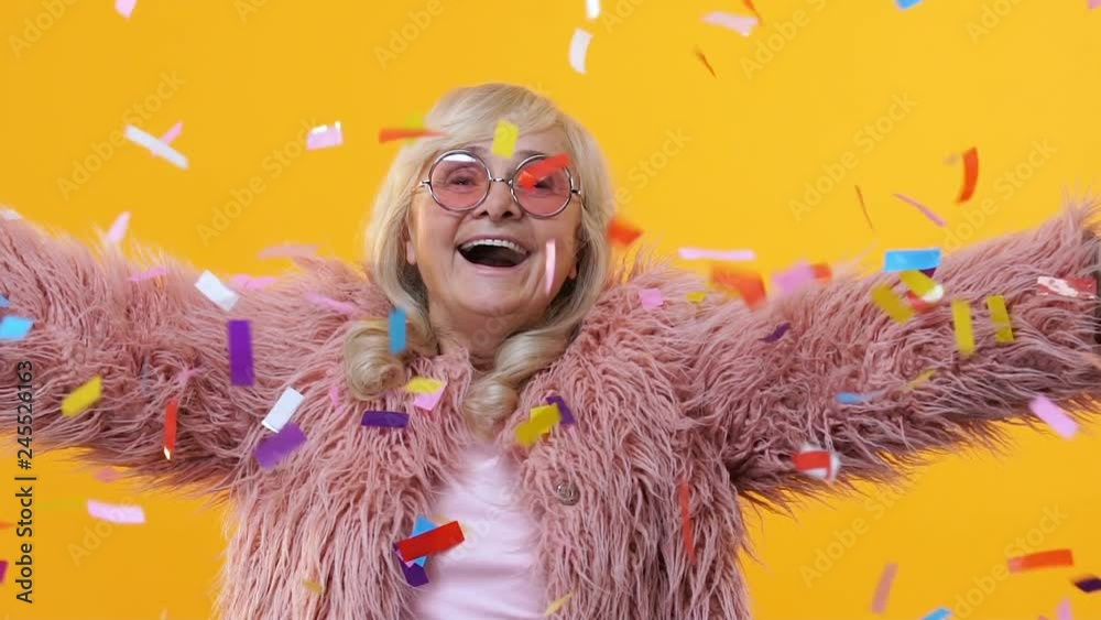 Cheerful senior woman stylish fur enjoying falling confetti, festival happiness
