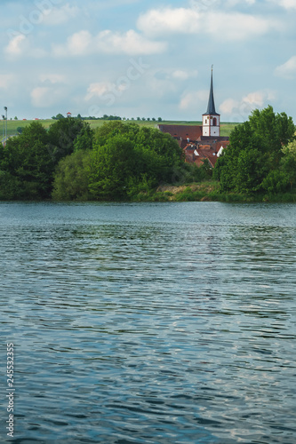 A Franconian German village landscape on a river. the church rises above the church. the old main in the foreground. a beautiful sky in the background. Rich green nature framed everything © René Bittner