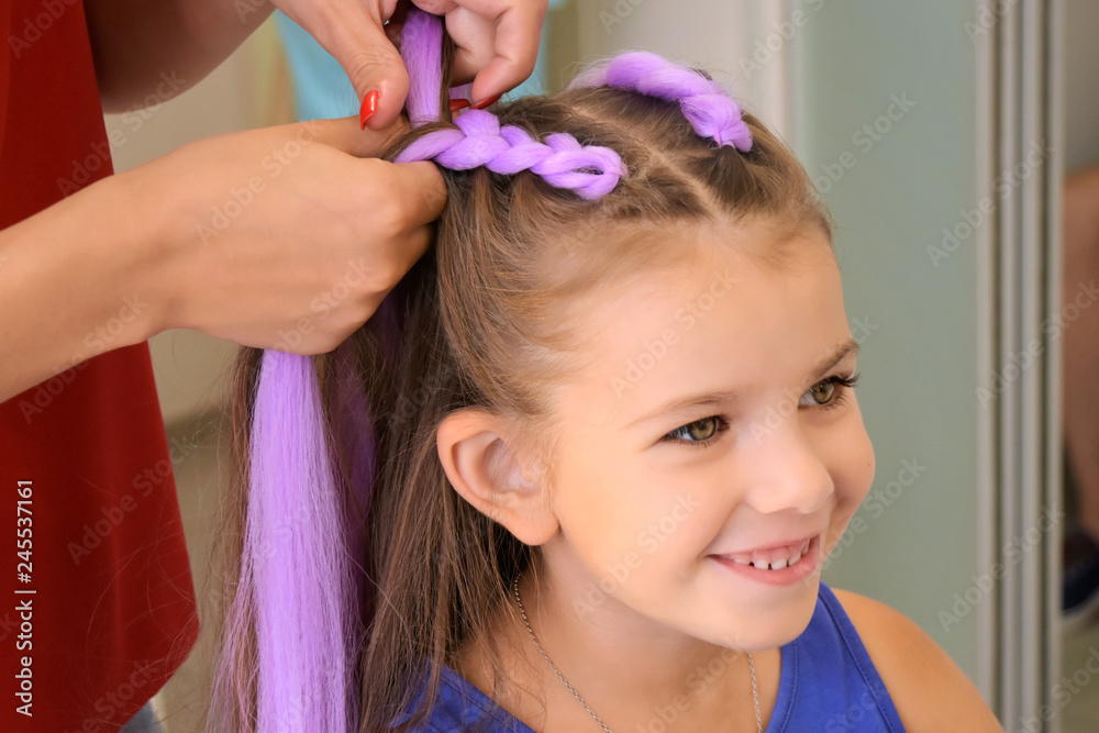 Beautiful caucasian white little girl at the professional hair salon.  Hairdresser making two stylish braids with violet kanekalon for smiling  adorable kid. Braided child hair with pony tails. Stock Photo | Adobe