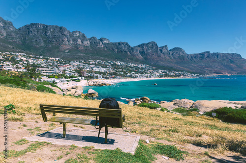 Backpack of lonely traveller on a bench with a view of Camps bay beautiful beach in Cape Town, South Africa