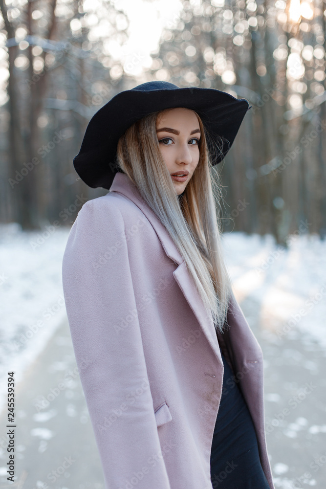 Pretty beautiful young woman in stylish winter glamor clothes goes in a chic  hat in a snowy forest on a winter sunny day. Fashionable attractive stylish  girl. Stock Photo