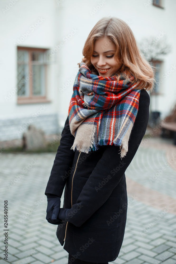 Young attractive woman in a stylish winter coat in black gloves in a  fashionable vintage wool scarf on the background of a white modern  building. Beautiful girl smiling Stock Photo | Adobe