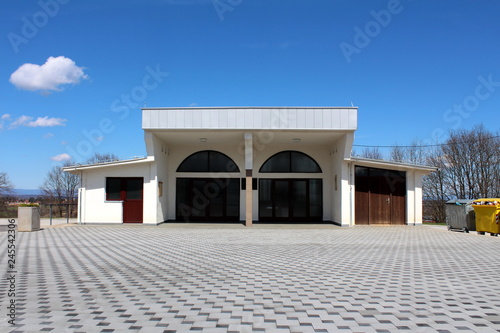 Renovated cemetery mortuary building with two rooms and storage area surrounded with modern stone tiles and trees without leaves with blue sky in background