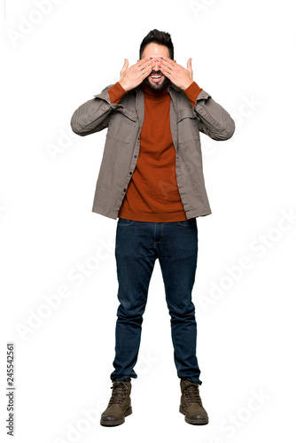 Full-length shot of Handsome man with beard covering eyes by hands. Surprised to see what is ahead on isolated white background
