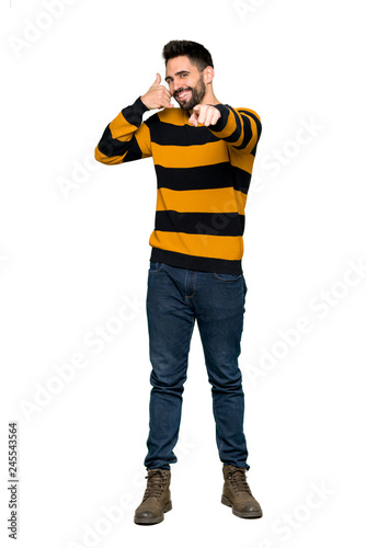 Full-length shot of Handsome man with striped sweater making phone gesture and pointing front on isolated white background