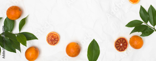 many fresh blood oranges and green leaves on white crumpled paper background