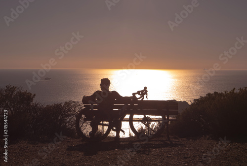 The young man with bicycle sitting on a mountain watching the sunset